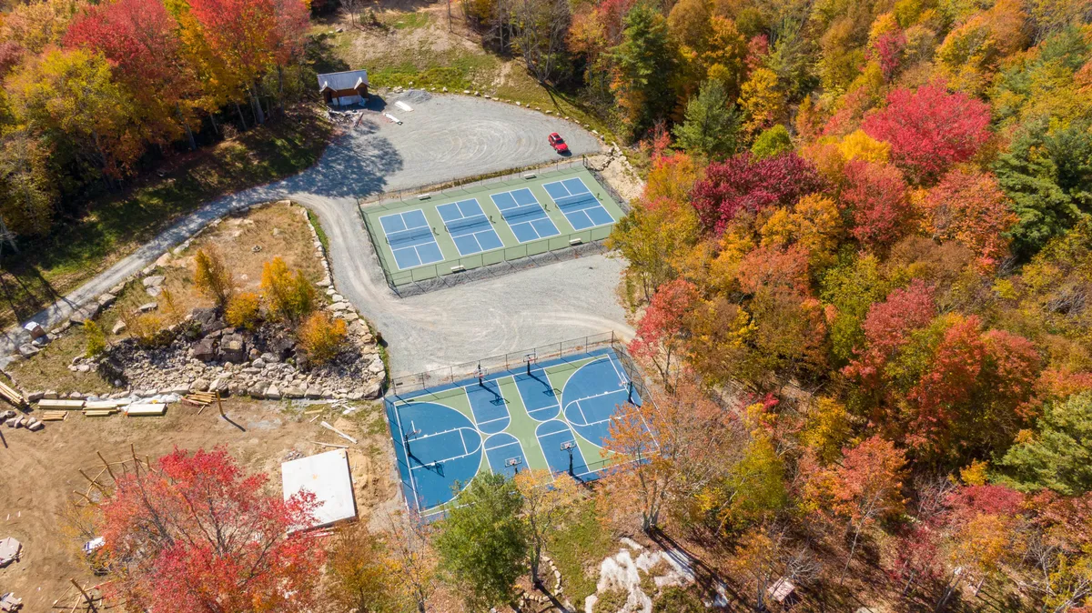 A bright, dynamic view of the community’s sports complex, featuring both basketball and tennis courts, surrounded by vibrant autumn foliage. The space is energetic and well-suited to group activities, echoing the appeal for families, active adults, and social groups.