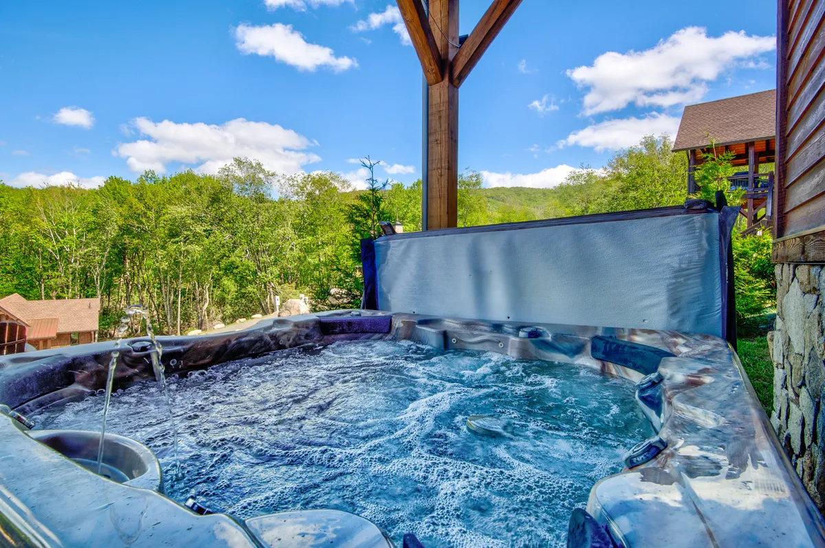A bubbling hot tub set outdoors amidst trees, under a clear blue sky. The setting emphasizes relaxation and soaking in nature, with the possibility of enjoying sunset views or stargazing from the water.