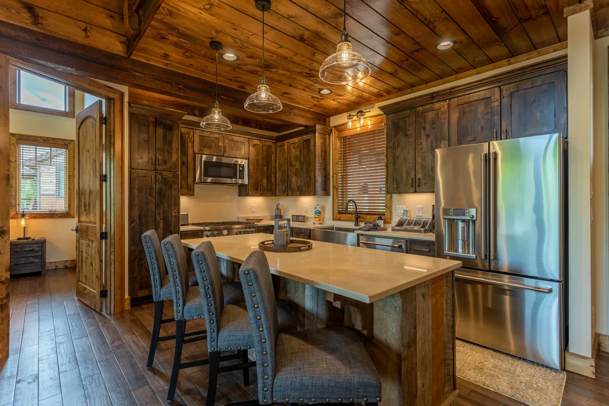 The kitchen is the focal point here, with a stylish island, stainless steel appliances, wooden cabinetry, and hanging light fixtures. Large enough for group cooking or casual dining, the space exudes an upscale yet welcoming ambiance.