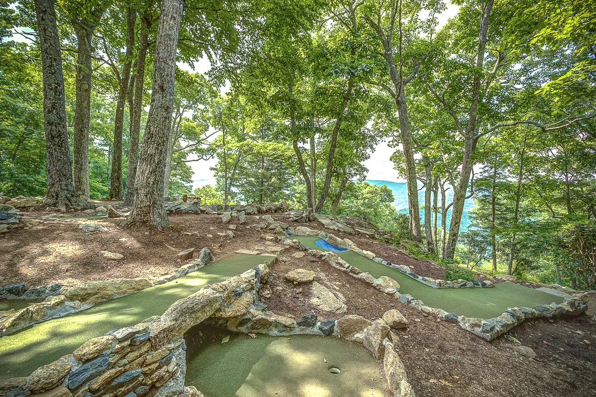 A playful mini-golf course set amid natural stone features and surrounded by tall trees, inviting families or groups to relax and have fun together outdoors.