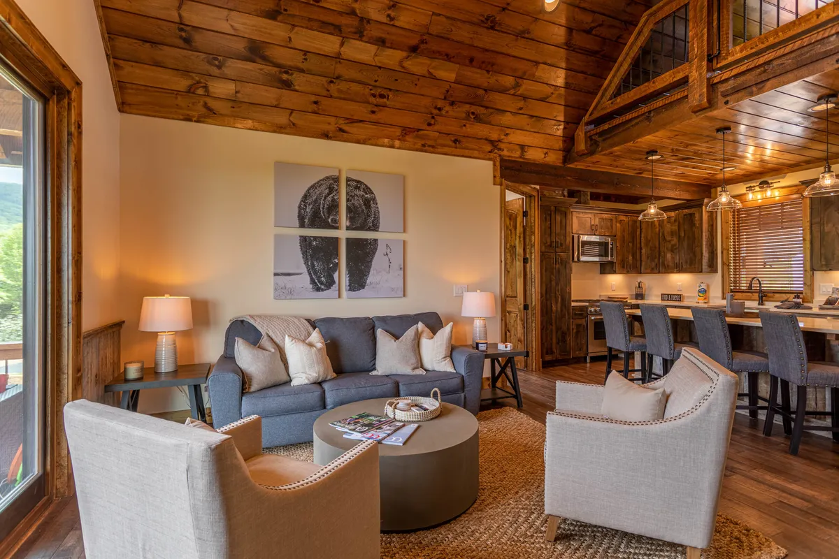 A cozy seating area blends seamlessly into the open kitchen, with a plush sofa and armchairs facing each other and stylish artwork adorning the walls. The kitchen area is in clear view, reinforcing the sense of togetherness and interaction.