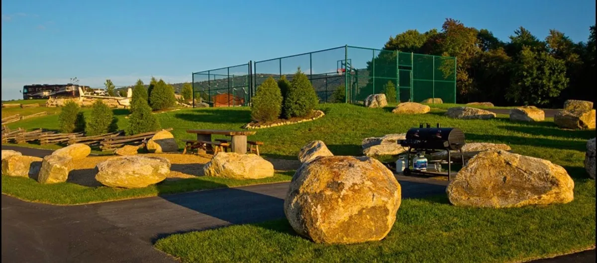 A large boulder-studded area with a tennis court, grill area, and picnic table highlights active community amenities. The setting suggests opportunities for friendly competitions, picnics, and outdoor gatherings in a scenic environment.