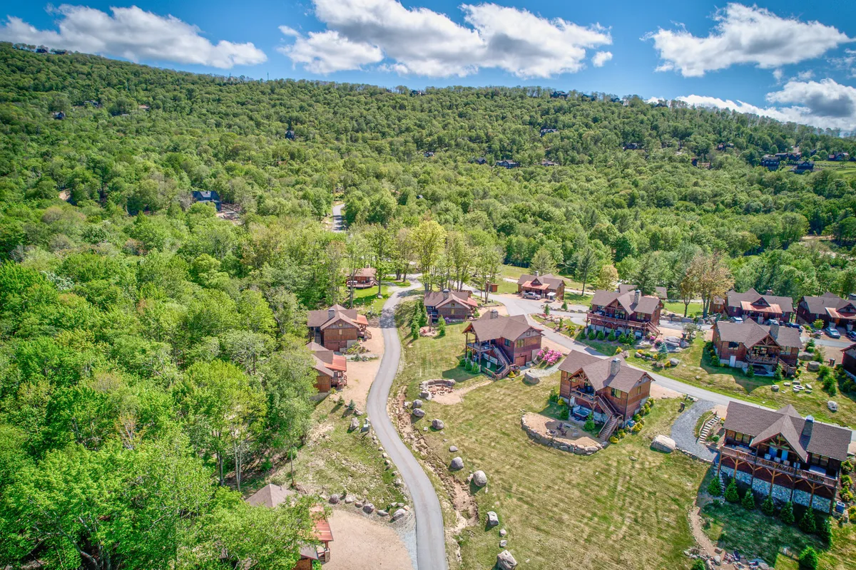 A relaxed exterior view with a cluster of cabins, a winding road, and surrounding greenery. The setting is ideal for hiking, outdoor gatherings, and enjoying community events, with plenty of shared space for families and groups.