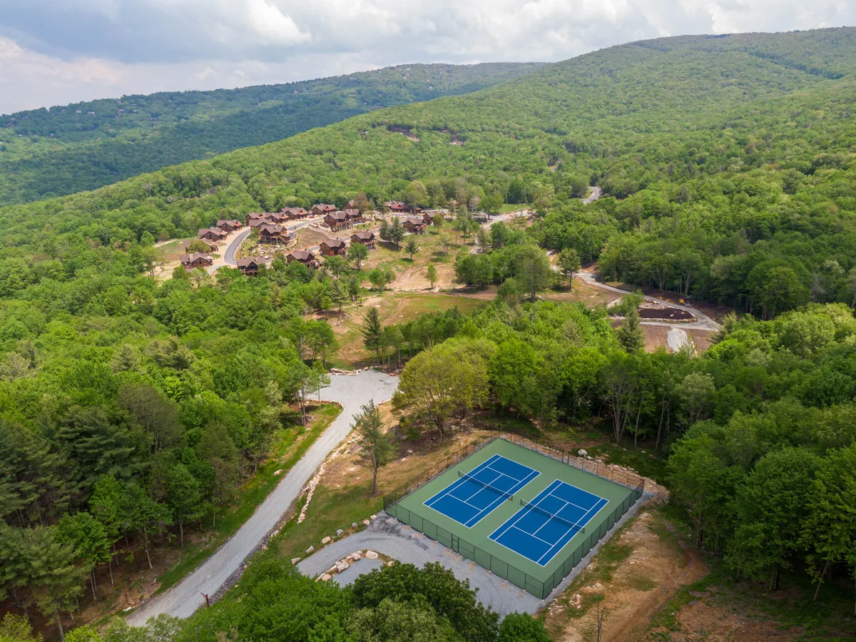 A wide shot of tennis courts set against a mountainous landscape with nearby residential buildings, inviting an active lifestyle. The open courts evoke opportunities for various sports and recreation with family and friends.