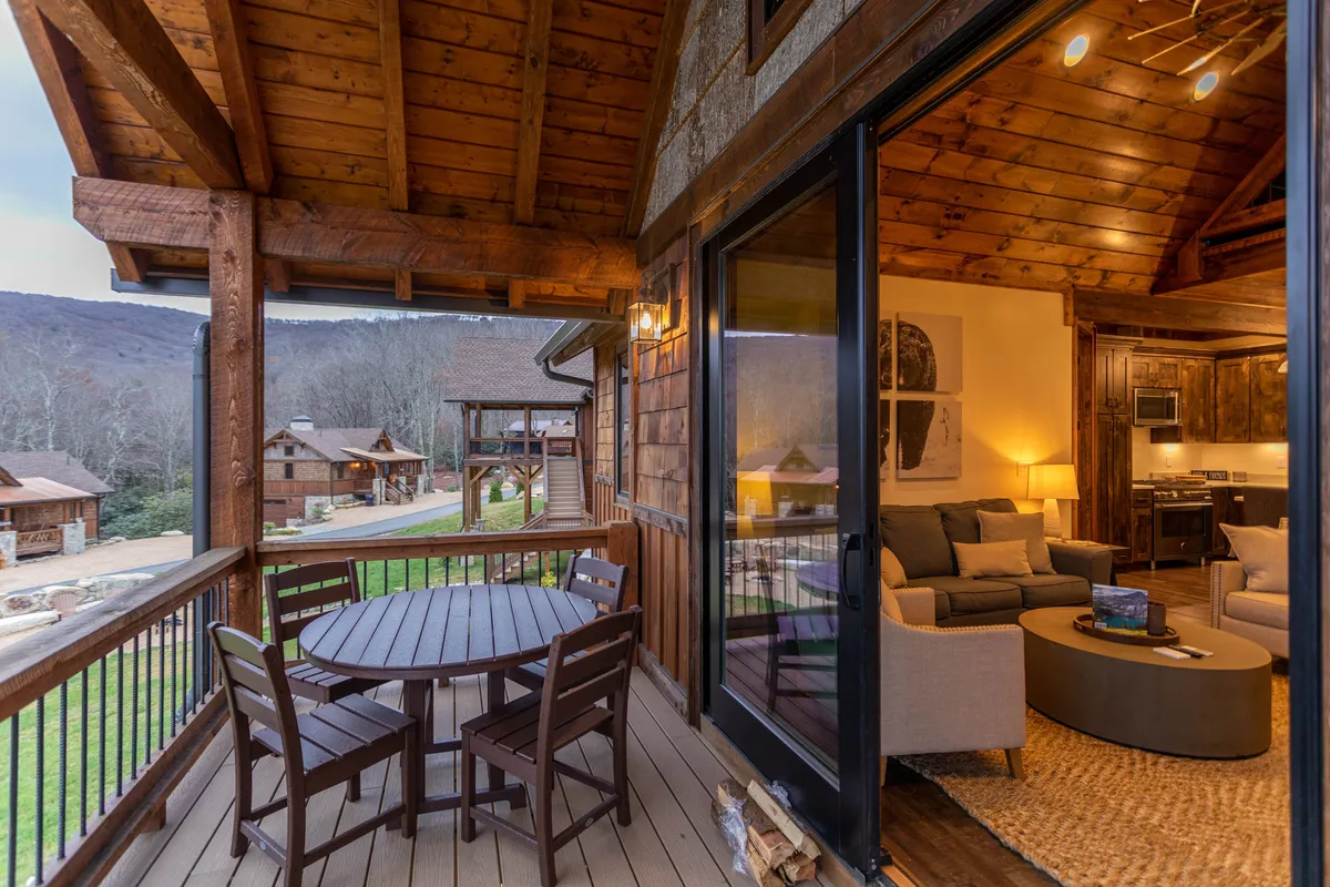 A spacious wooden deck with a round dining table and comfortable seating, all oriented toward a sweeping mountain view. The scene suggests relaxation, outdoor meals, and panoramic vistas, with natural light enhancing the tranquil, welcoming mood.